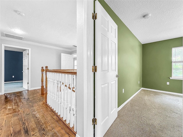 hallway featuring ornamental molding, wood-type flooring, and a textured ceiling