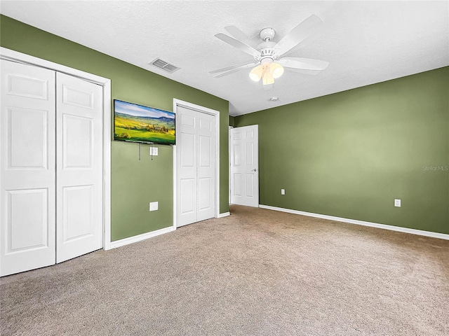 unfurnished bedroom featuring ceiling fan, a textured ceiling, carpet floors, and multiple closets