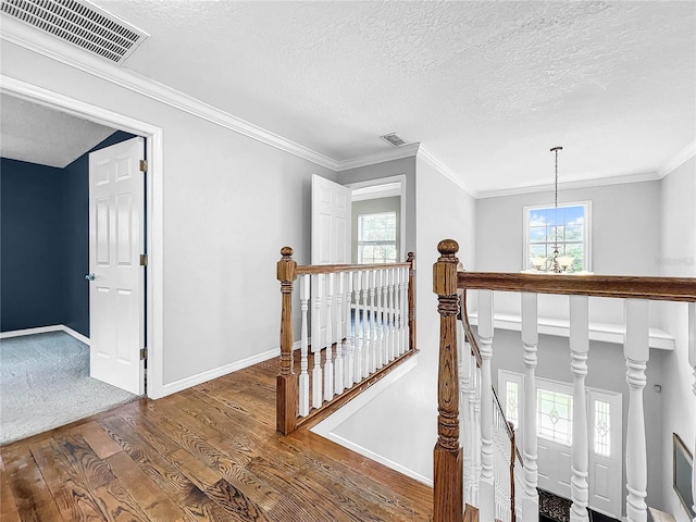 hall with an inviting chandelier, ornamental molding, wood-type flooring, and a textured ceiling