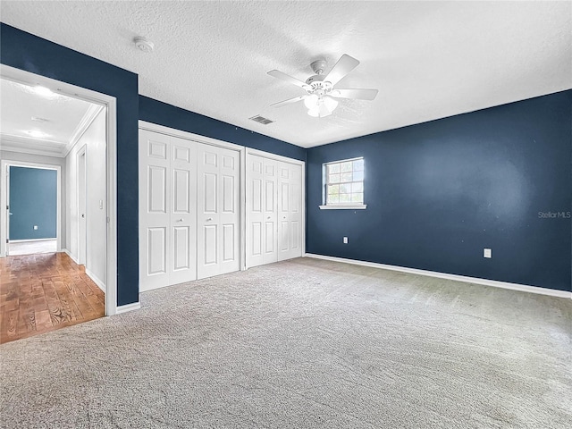 unfurnished bedroom featuring multiple closets, carpet flooring, a textured ceiling, and ceiling fan