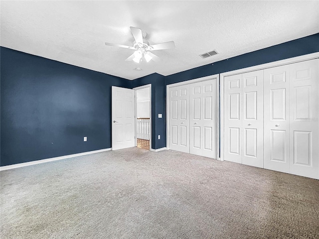 unfurnished bedroom featuring multiple closets, carpet, a textured ceiling, and ceiling fan