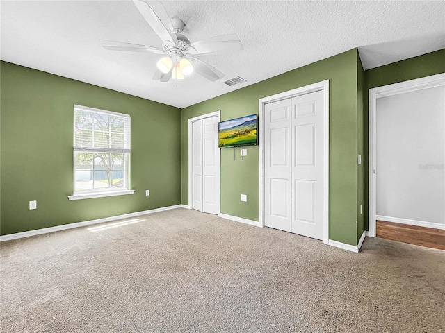 unfurnished bedroom featuring multiple closets, carpet, a textured ceiling, and ceiling fan