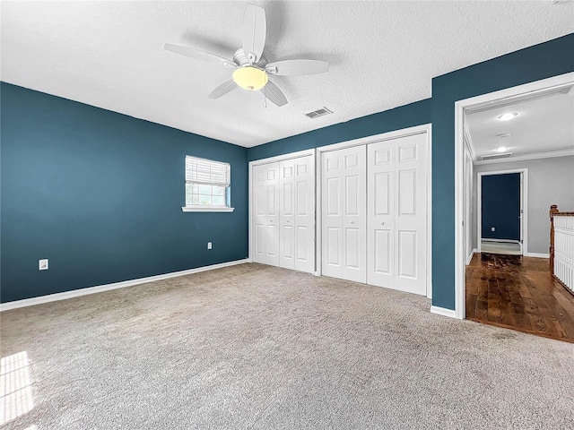 unfurnished bedroom featuring ceiling fan, carpet floors, a textured ceiling, and two closets