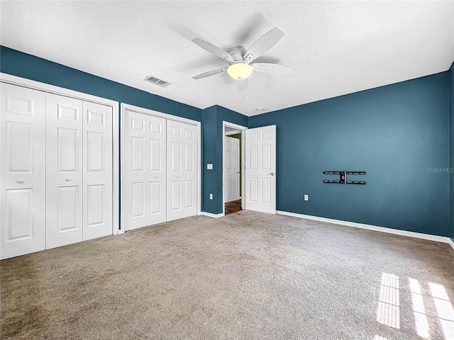 unfurnished bedroom featuring two closets, a textured ceiling, ceiling fan, and carpet flooring