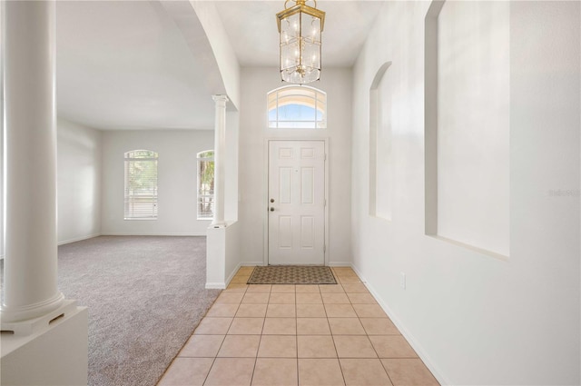 foyer featuring decorative columns, a chandelier, and light carpet