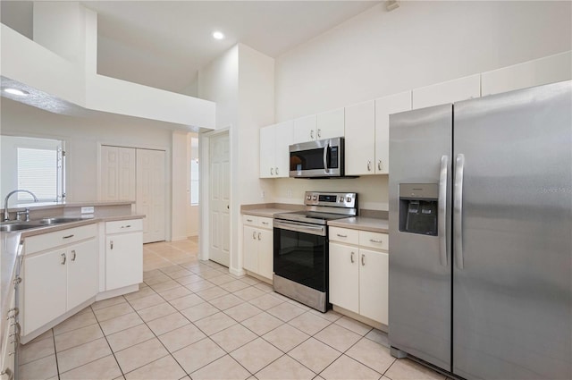 kitchen featuring sink, white cabinetry, light tile patterned floors, a high ceiling, and stainless steel appliances