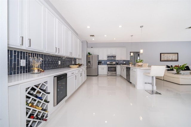 kitchen featuring appliances with stainless steel finishes, pendant lighting, wine cooler, white cabinets, and backsplash