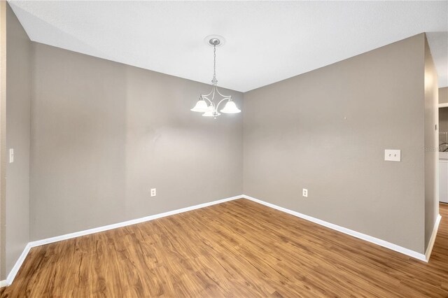 empty room with wood-type flooring and an inviting chandelier