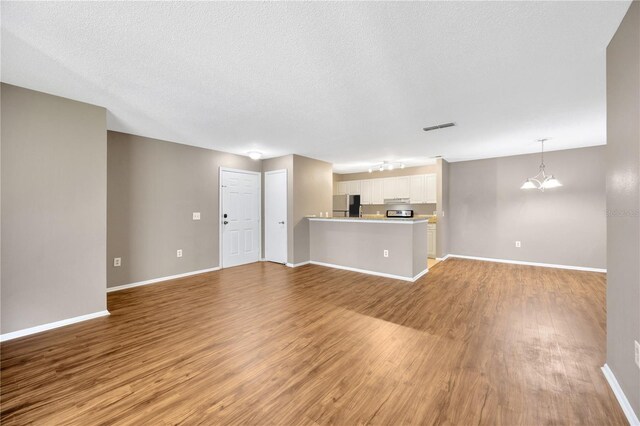 unfurnished living room with light hardwood / wood-style floors, a notable chandelier, and a textured ceiling