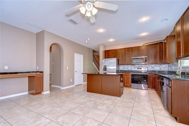 kitchen featuring stainless steel appliances, a sink, visible vents, a center island, and brown cabinetry