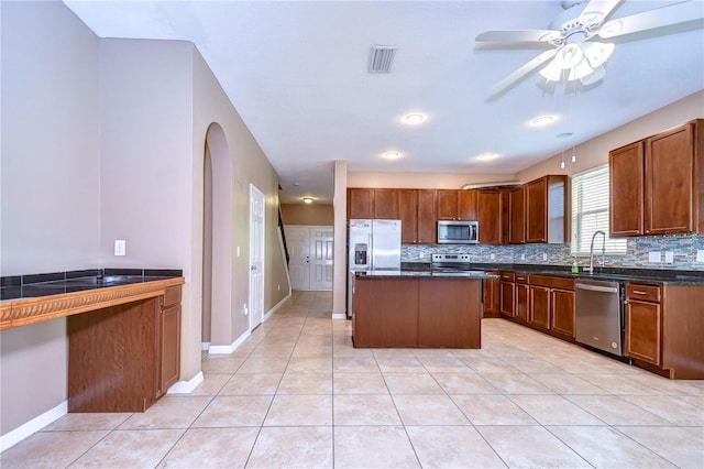 kitchen with a center island, stainless steel appliances, dark countertops, visible vents, and decorative backsplash