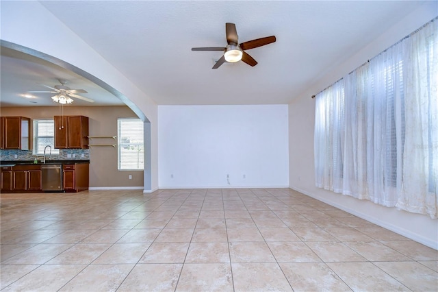 unfurnished living room featuring arched walkways, ceiling fan, baseboards, and light tile patterned floors