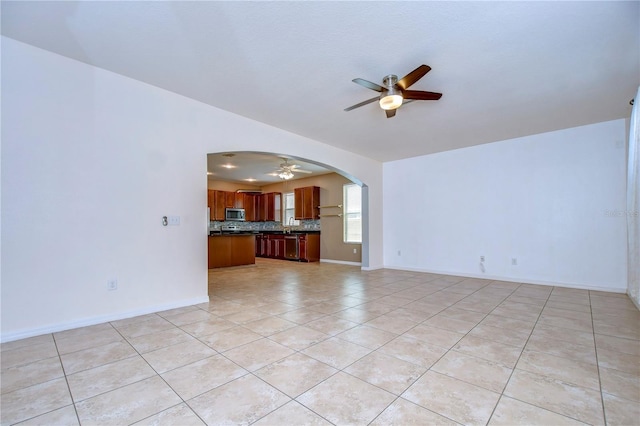 unfurnished living room featuring arched walkways, ceiling fan, light tile patterned floors, and baseboards