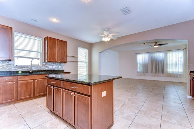 kitchen featuring visible vents, brown cabinetry, a kitchen island, a sink, and dark stone counters