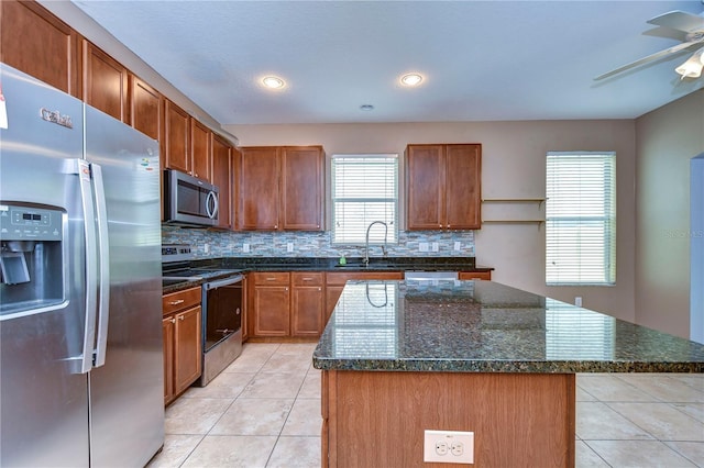 kitchen with a kitchen island, brown cabinets, stainless steel appliances, a sink, and light tile patterned flooring