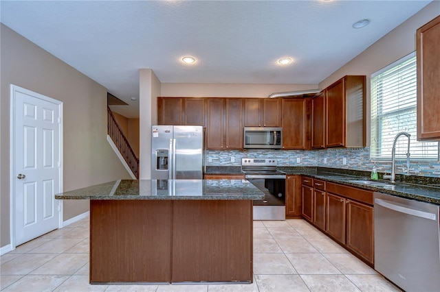 kitchen with a sink, stainless steel appliances, dark stone countertops, and a kitchen island