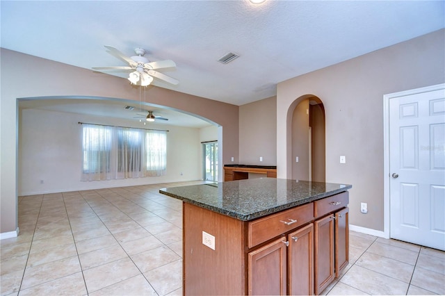 kitchen featuring visible vents, brown cabinetry, open floor plan, a kitchen island, and dark stone counters