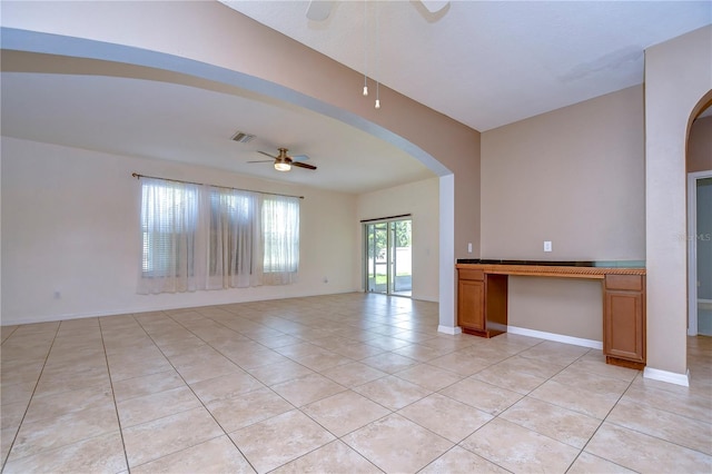 empty room with light tile patterned floors, baseboards, arched walkways, and a ceiling fan