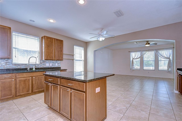 kitchen featuring visible vents, brown cabinetry, arched walkways, dark stone counters, and a kitchen island