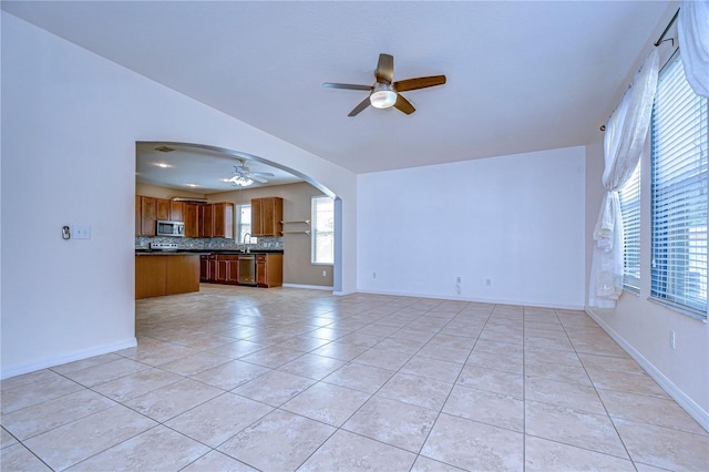 unfurnished living room featuring light tile patterned floors, baseboards, arched walkways, and a ceiling fan