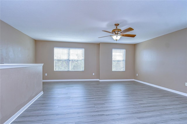 empty room with a ceiling fan, baseboards, a wealth of natural light, and wood finished floors