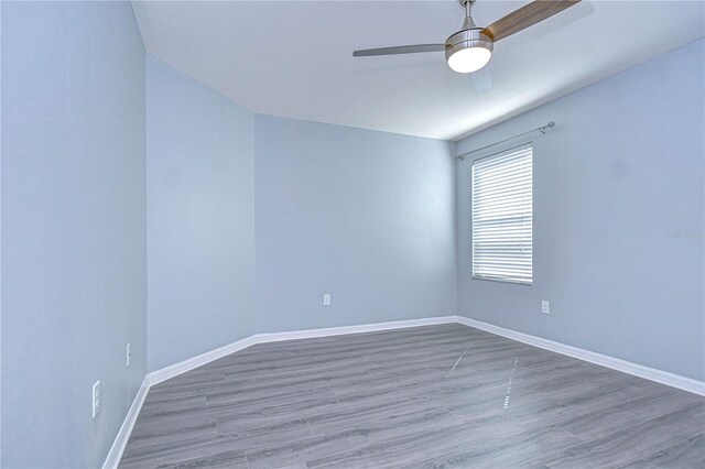 spare room with wood finished floors, a ceiling fan, and baseboards