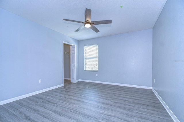 empty room featuring wood finished floors, a ceiling fan, and baseboards