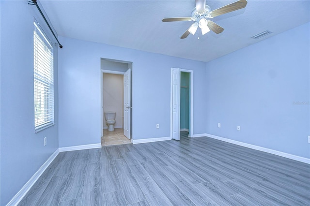 unfurnished bedroom featuring baseboards, visible vents, wood finished floors, and ensuite bathroom