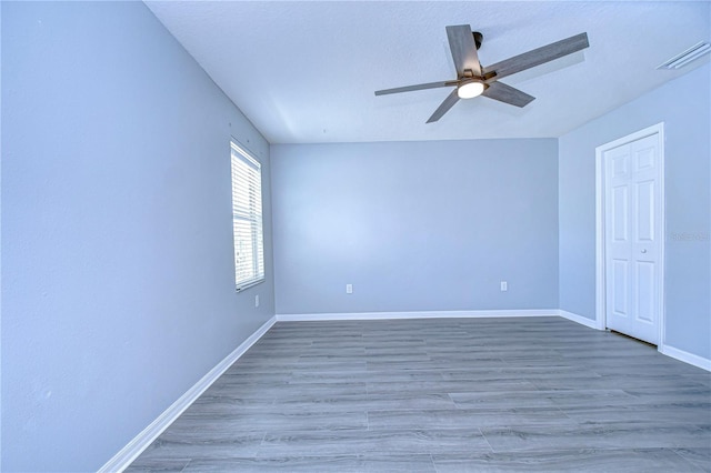 empty room featuring a ceiling fan, visible vents, baseboards, and wood finished floors