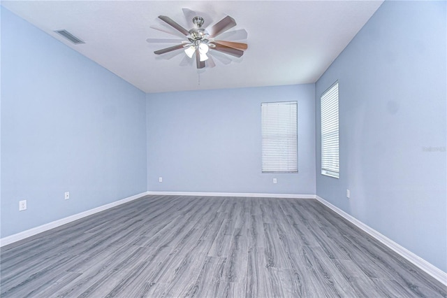 spare room with baseboards, wood finished floors, visible vents, and a ceiling fan