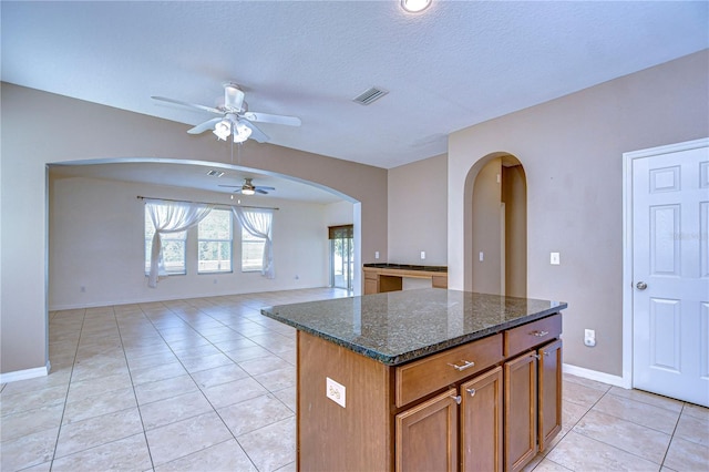 kitchen with a center island, visible vents, open floor plan, brown cabinets, and dark stone countertops