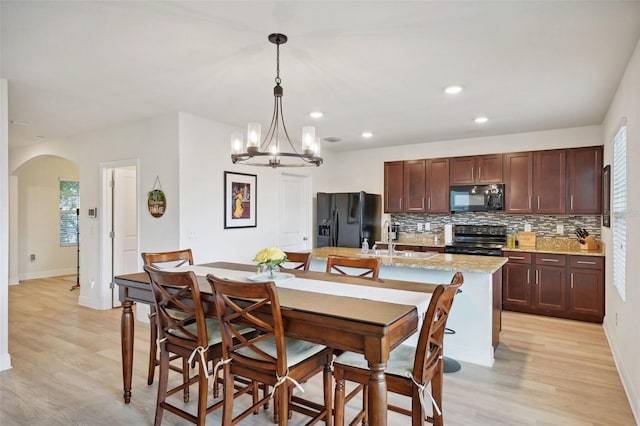 kitchen with a center island with sink, decorative light fixtures, a chandelier, black appliances, and sink