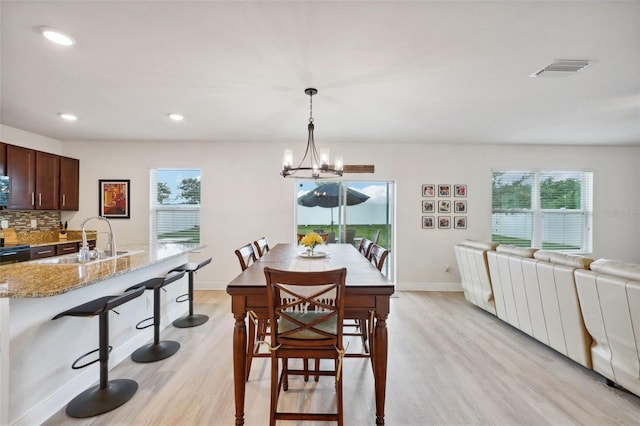 dining area with a healthy amount of sunlight, light wood-type flooring, sink, and an inviting chandelier