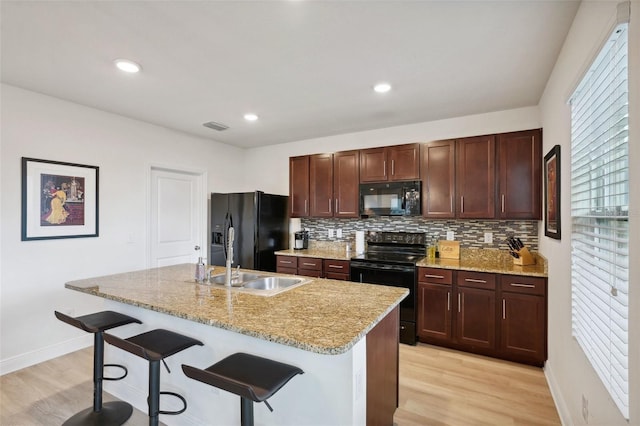 kitchen with a center island with sink, a kitchen breakfast bar, black appliances, light hardwood / wood-style flooring, and sink