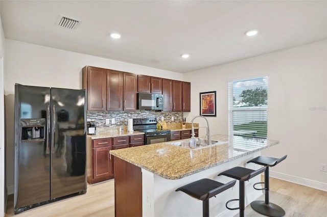 kitchen with black appliances, light hardwood / wood-style flooring, sink, a kitchen breakfast bar, and a center island with sink