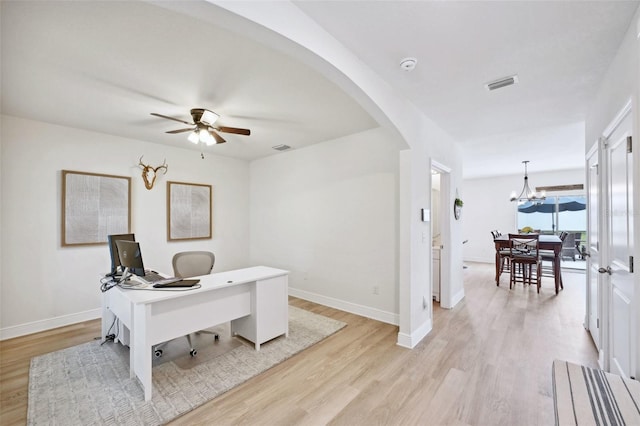 home office with ceiling fan with notable chandelier and light hardwood / wood-style floors