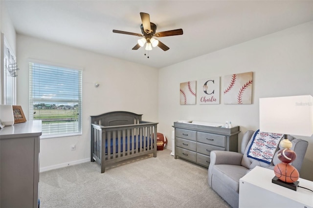 bedroom featuring ceiling fan, light colored carpet, and a nursery area