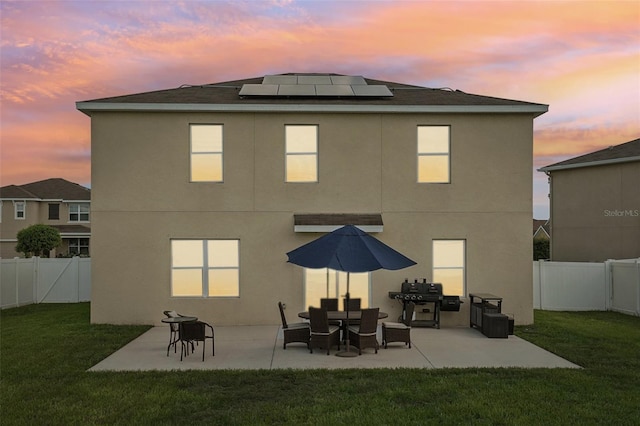 back house at dusk featuring a yard, solar panels, and a patio