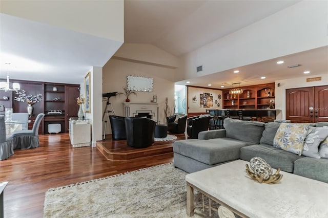 living room featuring hardwood / wood-style flooring, vaulted ceiling, built in shelves, and a chandelier