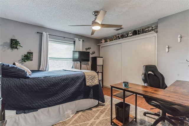 bedroom with a textured ceiling, a closet, ceiling fan, and light wood-type flooring