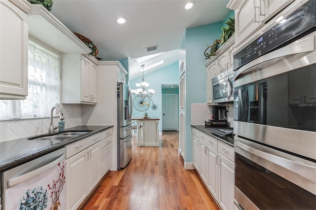 kitchen featuring vaulted ceiling, tasteful backsplash, white cabinetry, sink, and stainless steel appliances