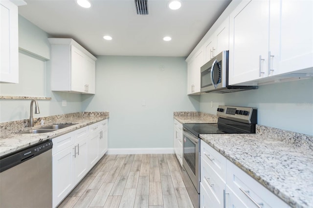 kitchen with white cabinets, light stone counters, stainless steel appliances, light hardwood / wood-style floors, and sink