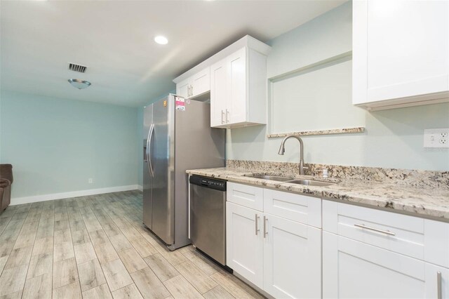 kitchen featuring sink, light hardwood / wood-style floors, stainless steel dishwasher, light stone countertops, and white cabinetry