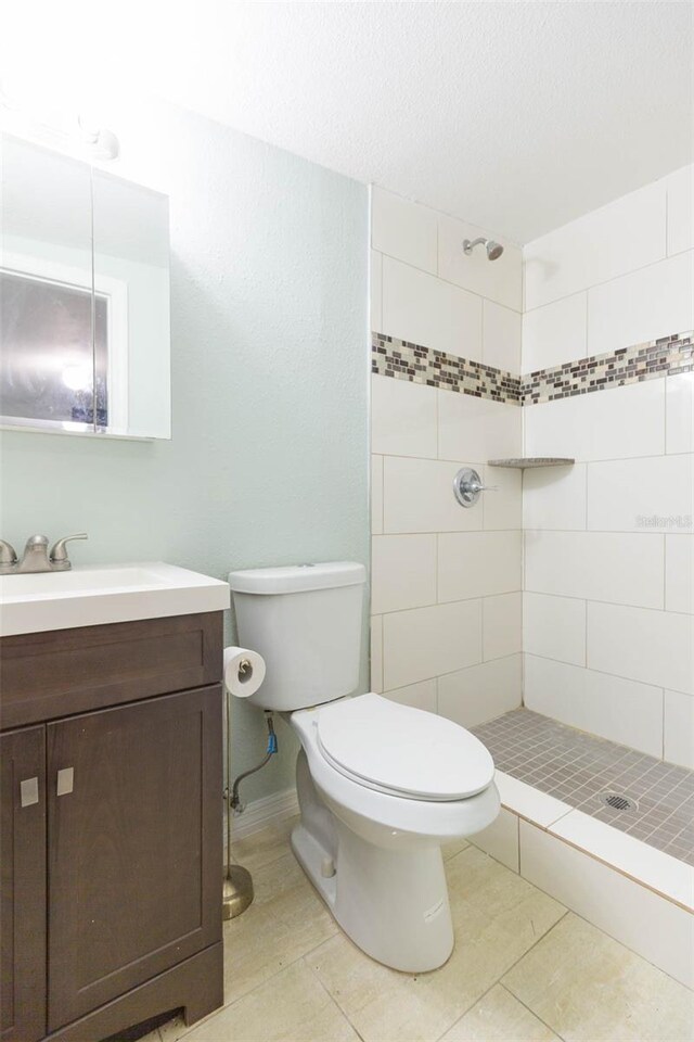 bathroom featuring vanity, tiled shower, tile patterned flooring, and toilet