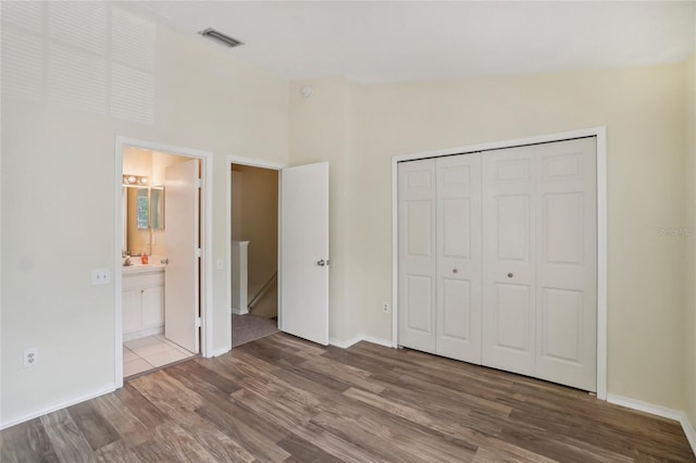 unfurnished bedroom with hardwood / wood-style flooring, connected bathroom, vaulted ceiling, and a closet