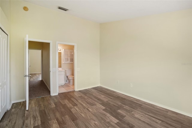 unfurnished bedroom with ensuite bathroom, dark hardwood / wood-style flooring, and a towering ceiling