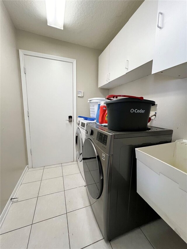 washroom with cabinets, a textured ceiling, sink, washing machine and clothes dryer, and light tile patterned flooring