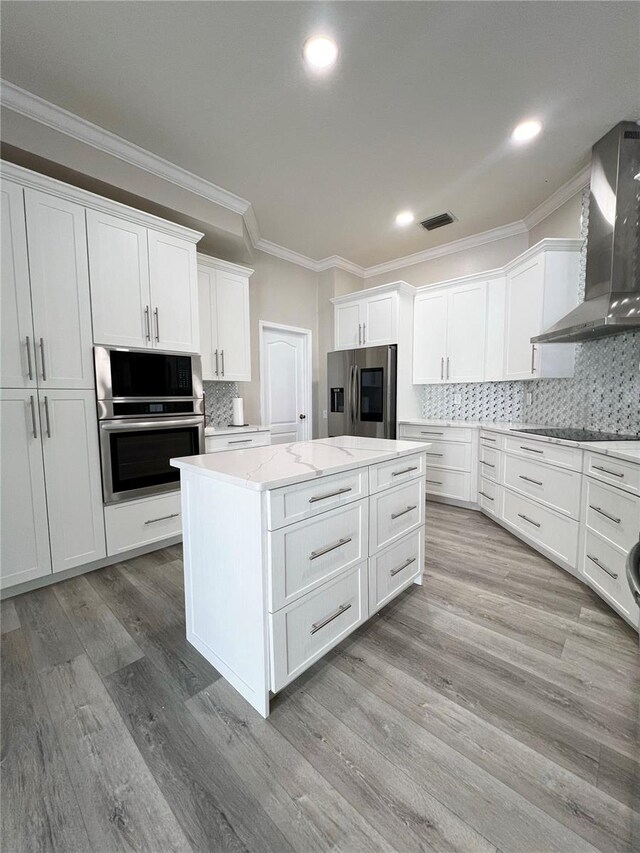 kitchen featuring white cabinetry, appliances with stainless steel finishes, tasteful backsplash, wall chimney exhaust hood, and a kitchen island