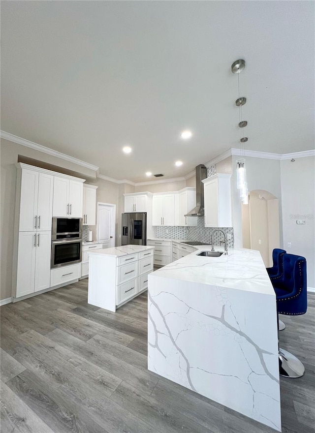 kitchen with light hardwood / wood-style flooring, hanging light fixtures, wall chimney range hood, backsplash, and appliances with stainless steel finishes