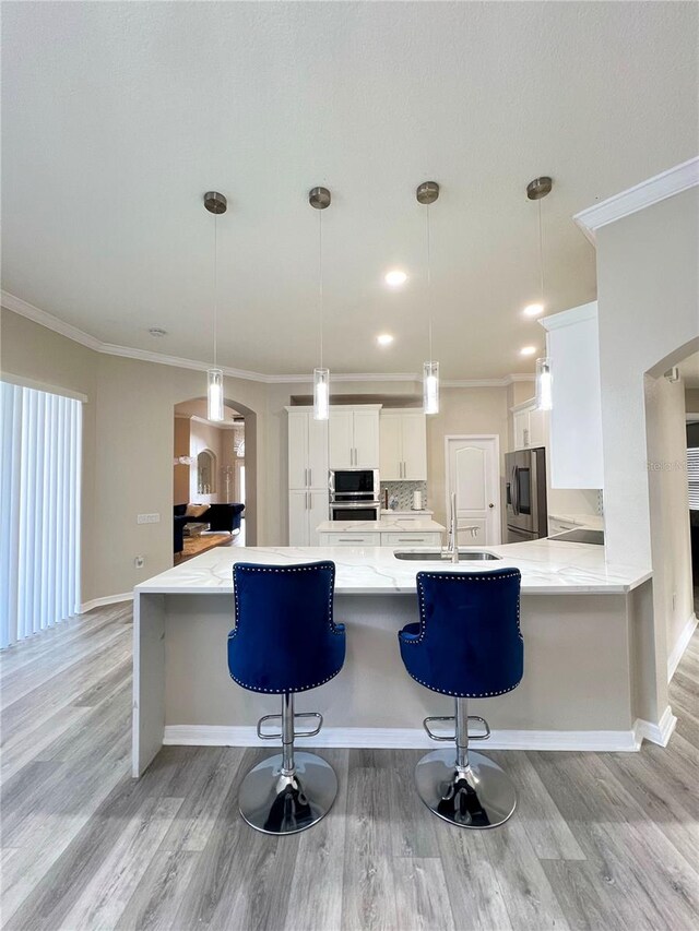 kitchen with sink, white cabinetry, light wood-type flooring, appliances with stainless steel finishes, and decorative light fixtures